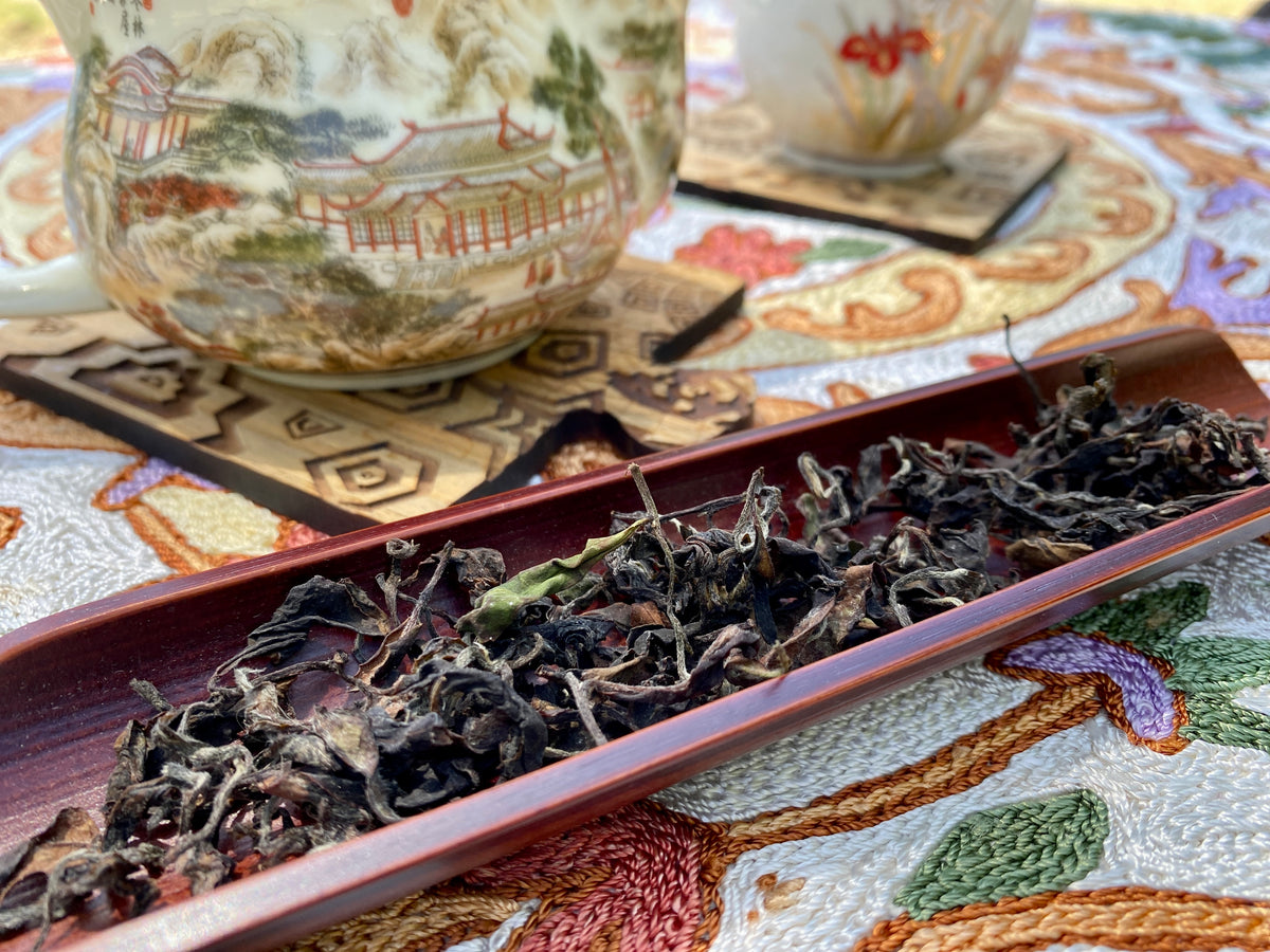 Loose leaf tea with teapot and teacup on a woven mat